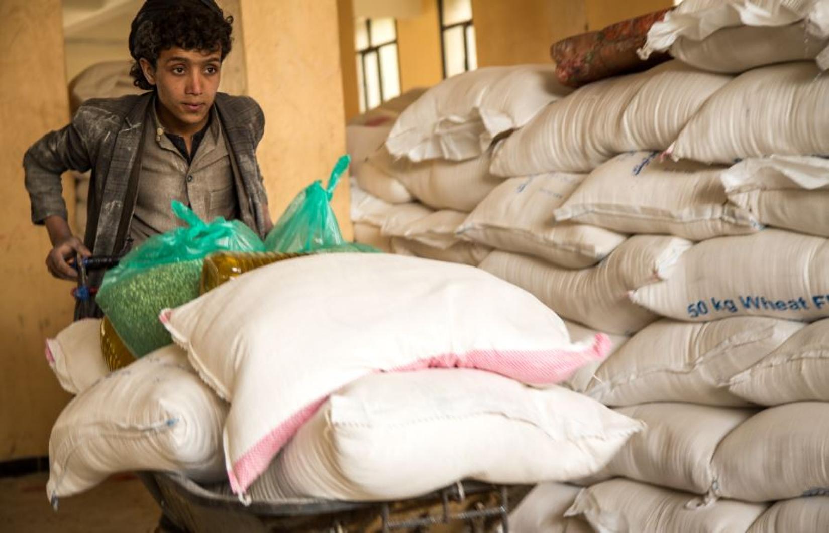 A boy pushes a wheelbarrow containing food rations